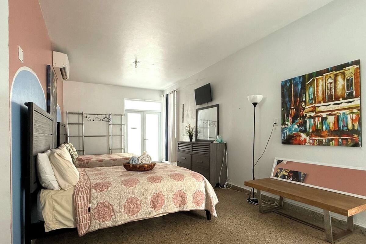 Ett sovrum med två sängar, en byrå, en bänk, en tavla och en tv på väggen.