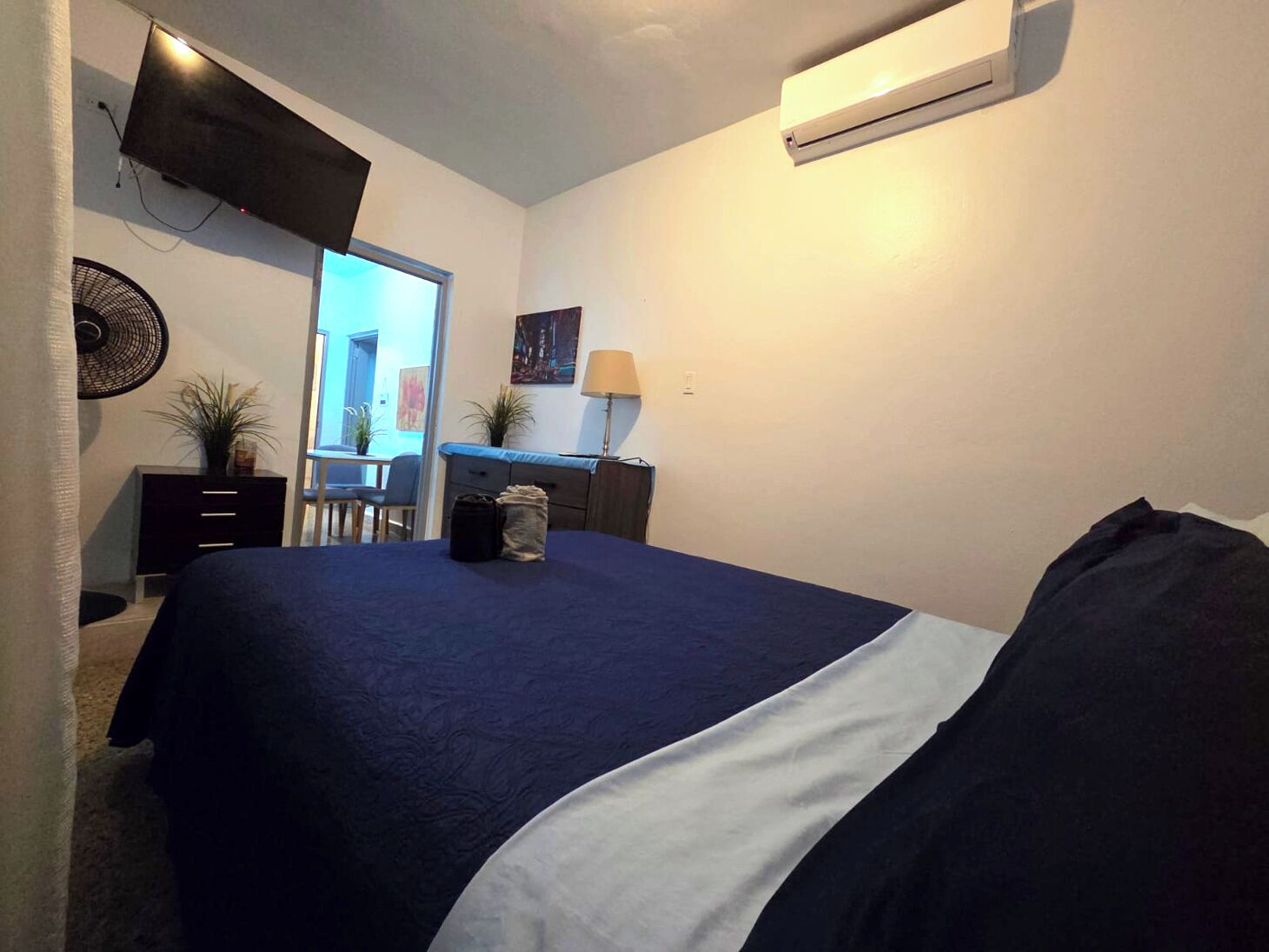 Ein Schlafzimmer mit Bett, Schreibtisch, Stuhl, Ventilator, Lampe und Klimaanlage.