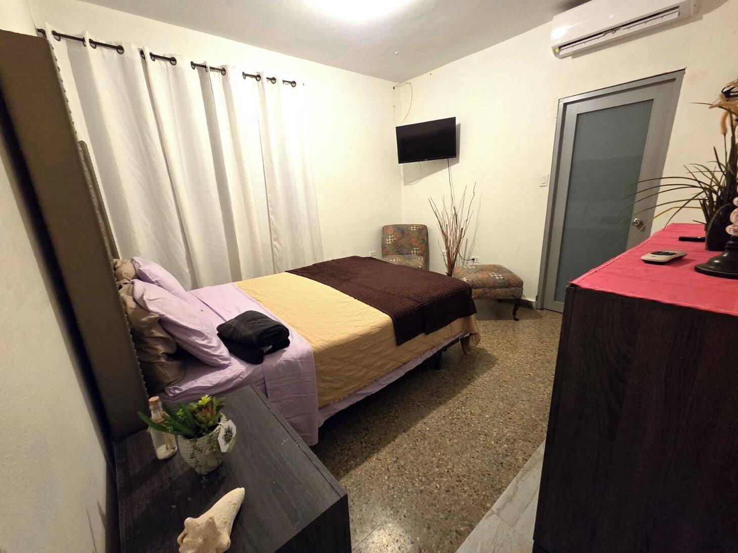 Ein Schlafzimmer mit einem Bett, einem Schreibtisch, einem Stuhl, einem Fernseher und einer Tür.