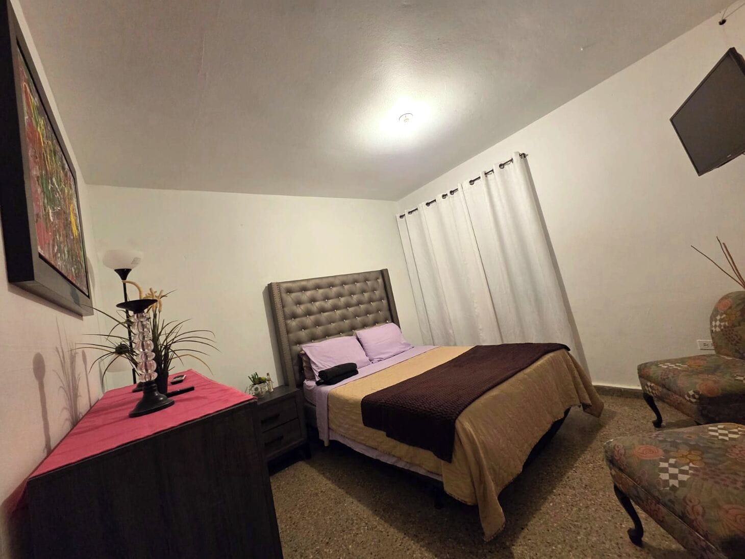 A bedroom with a bed, a desk, a chair, and a painting on the wall.