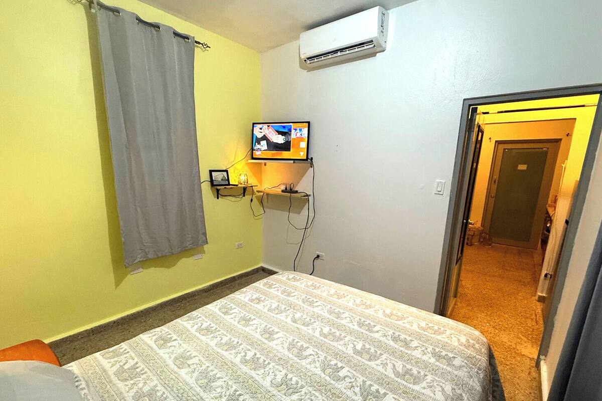 Ett hotellrum med en säng, en tv som är monterad på väggen och en luftkonditioneringsanläggning.