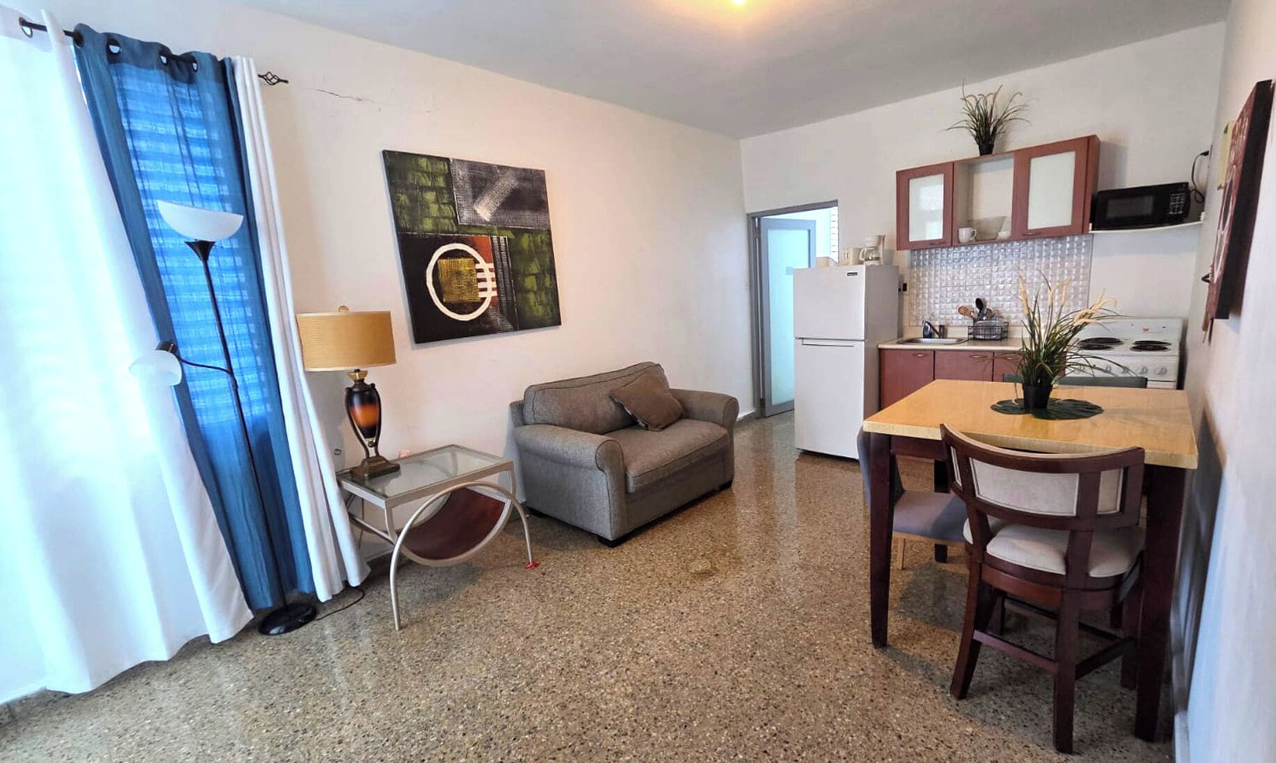 Un espacio habitable compacto con kitchenette, un sofá, una mesa de comedor con sillas y una lámpara.