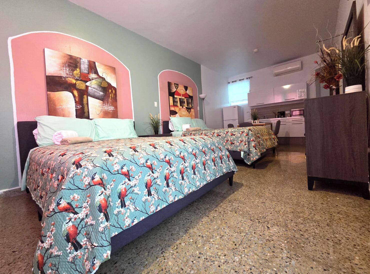 A bedroom with two beds, a kitchenette, and a bathroom.