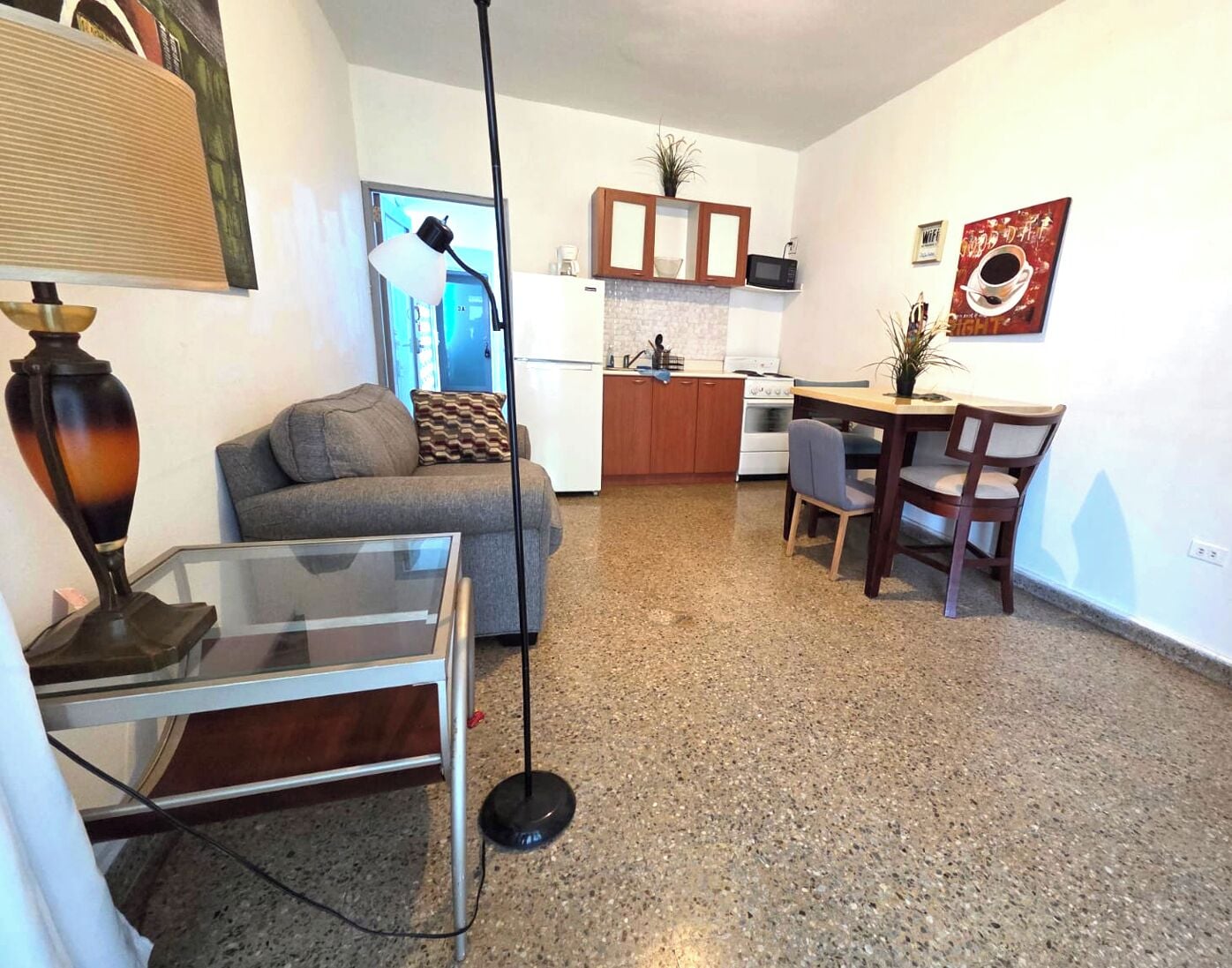 A compact living space with a sofa, a dining table with chairs, a kitchen area with a microwave and stove, and a floor lamp.
