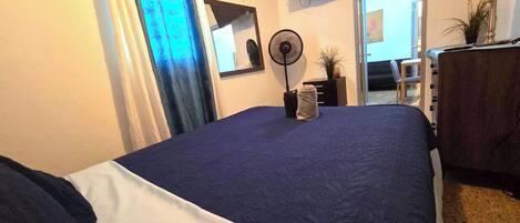 Habitación de hotel con una cama, un televisor montado en la pared, un escritorio con lámpara y una ventana con cortinas.