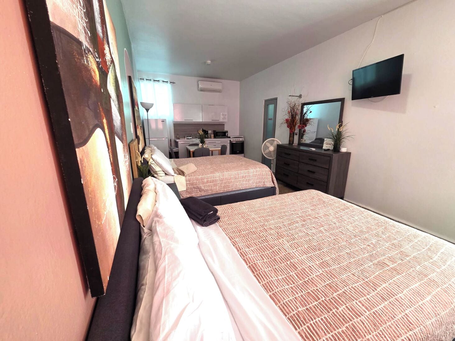 Une chambre d’hôtel avec deux lits, une kitchenette, une télévision et un miroir.
