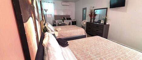 Une chambre d’hôtel avec deux lits, une kitchenette, une télévision et un miroir.