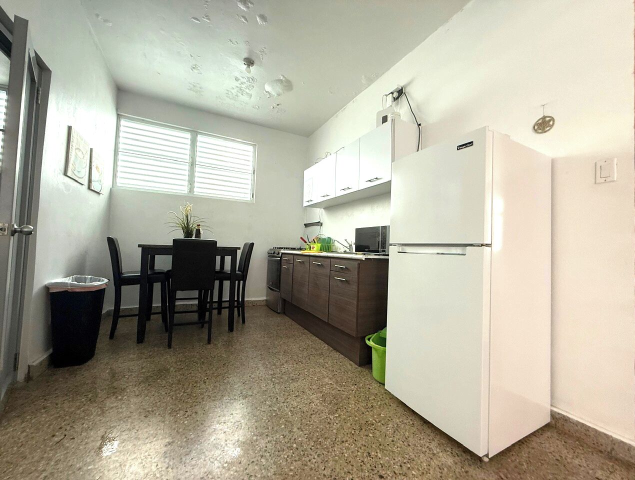 Una cocina compacta con una mesa de comedor, sillas, un refrigerador y armarios.