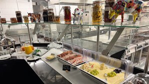 Ein reichhaltiges Buffet mit verschiedenen Speisen, darunter Fleisch, Käse und Obst, präsentiert in durchsichtigen Behältern.