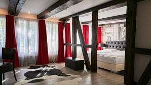 Ein Schlafzimmer mit einem Bett, einem Sessel, einem Kuhfellteppich und roten Vorhängen.
