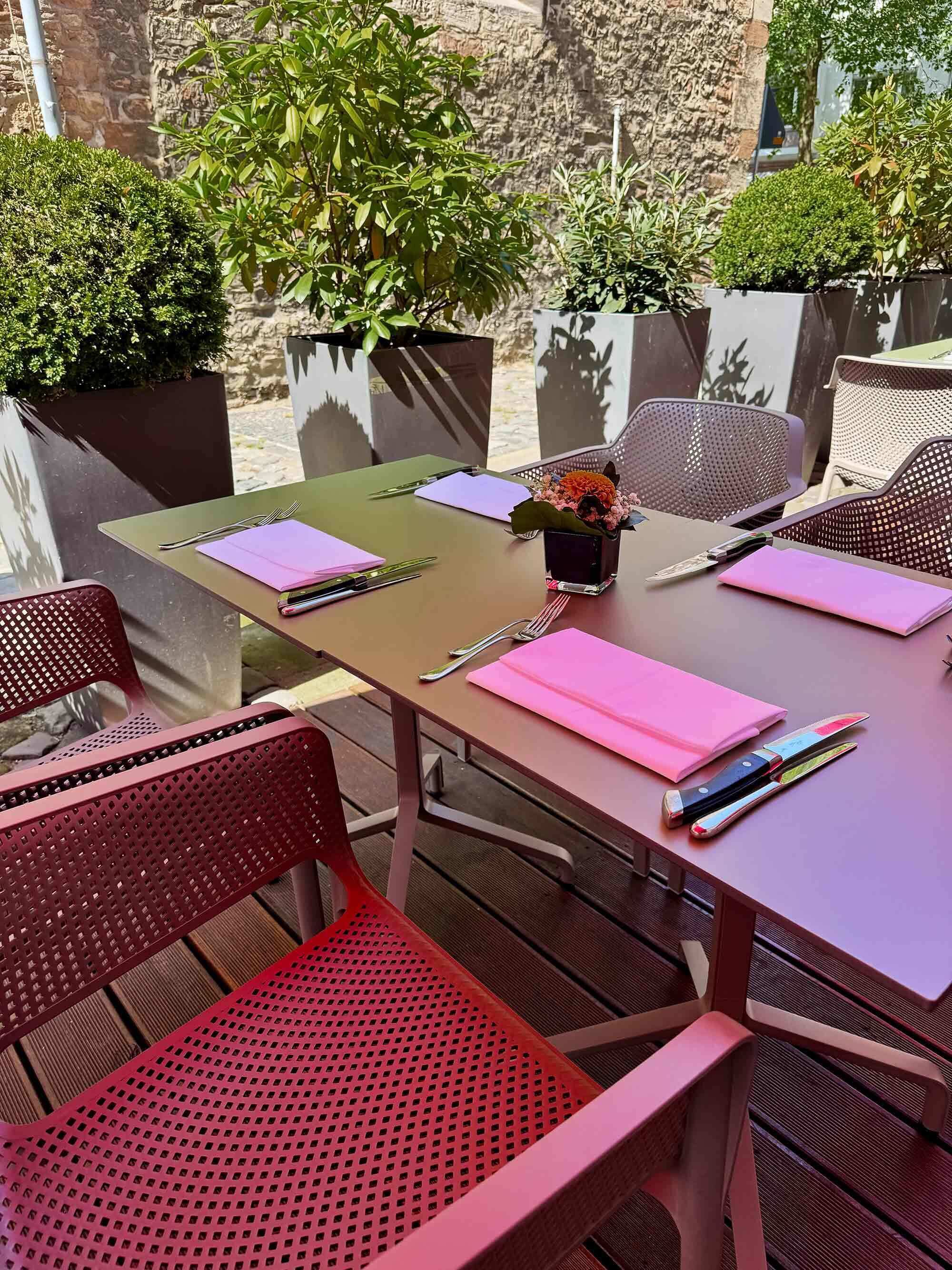 An outdoor dining area with a table set for two, surrounded by metal chairs, and potted plants.