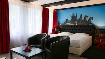 Una habitación de hotel con una cama, dos sillones de cuero negro, una mesita con manzanas, cortinas rojas y un mural de caballos en la pared.