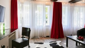 Ein Zimmer mit Glastisch, schwarzem Stuhl, Kuhfellteppich und roten Vorhängen.