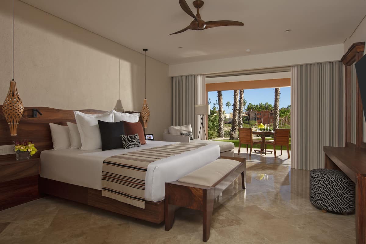 A spacious bedroom with a large bed, a wooden headboard, a ceiling fan, and a view of the outdoor patio.