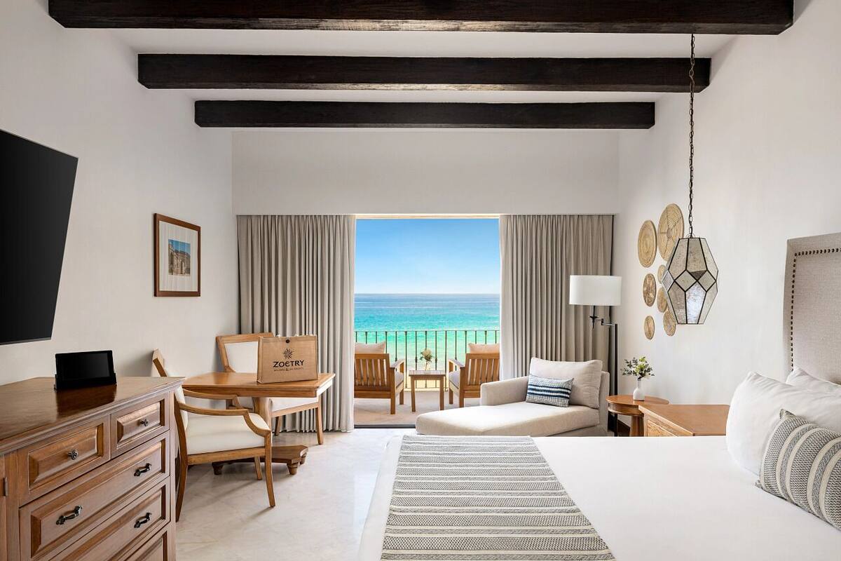 A hotel room with a bed, a desk, a chair, a table, and a view of the ocean.