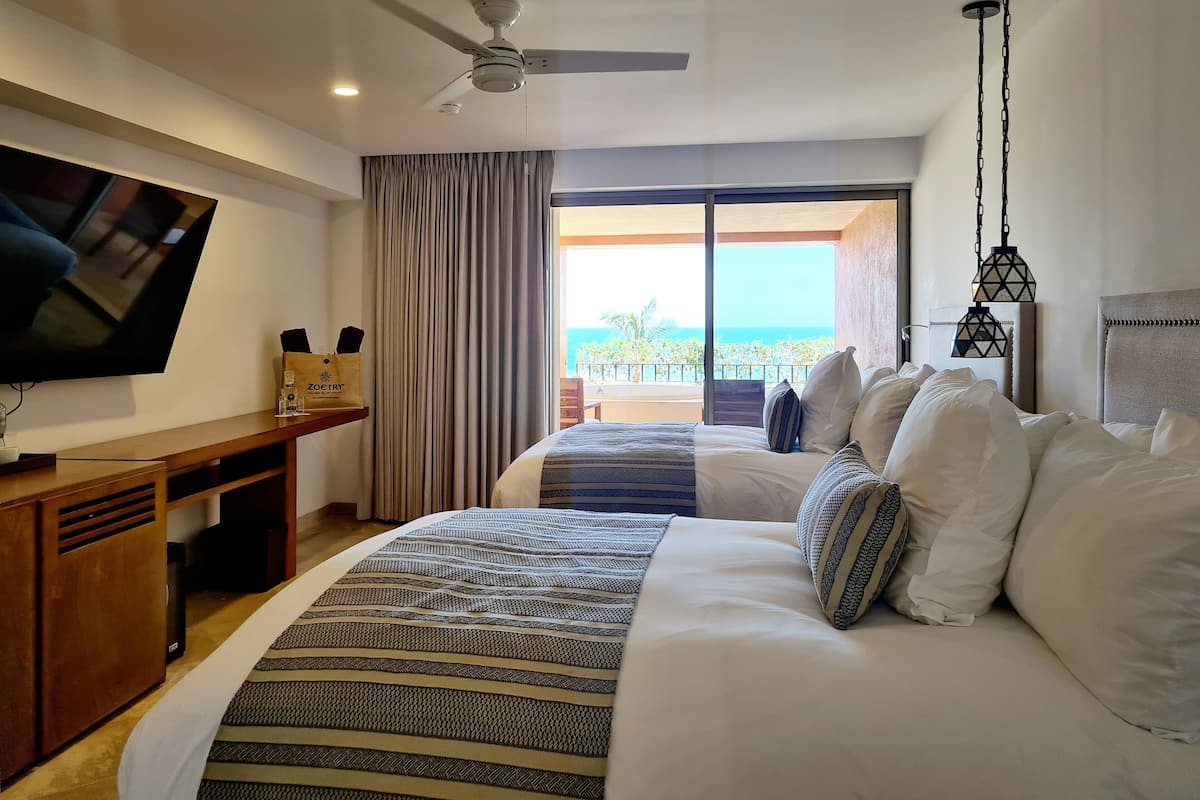 A hotel room with a bed, a desk, a television, and a view of the ocean.