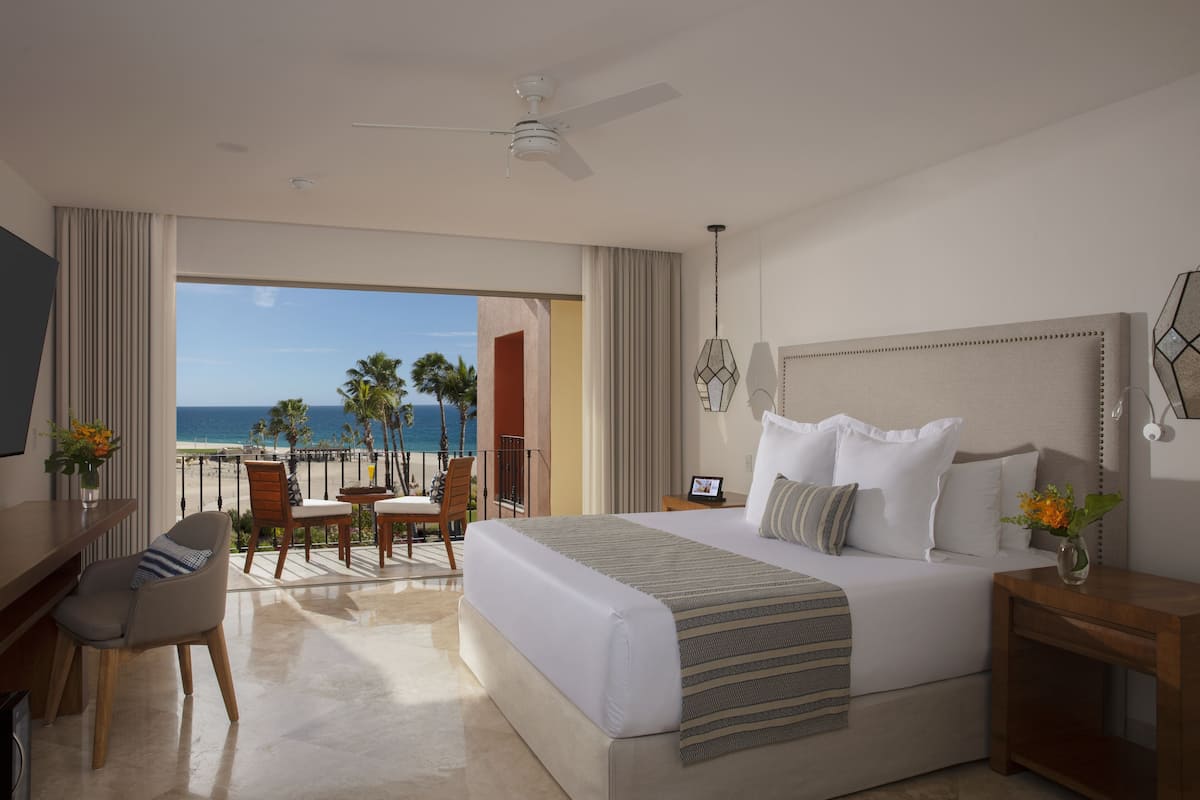 A hotel room with a large bed, a desk, a chair, and a view of the beach.