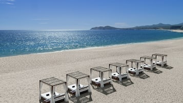 Una playa con sillones blancos y mesas dispuestas en fila.