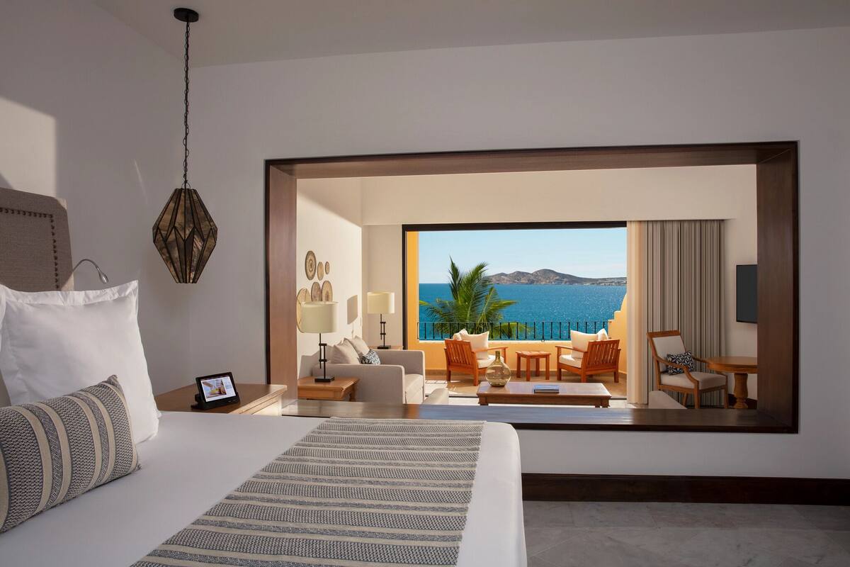 A hotel room with a large bed, a nightstand, a desk, a chair, a table, and a view of the ocean.