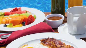 Un desayuno con un plato de huevos, tocino y salchichas, un plato de fruta y dos bebidas.