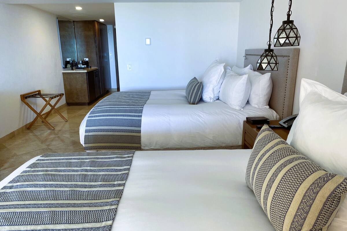 A hotel room with two beds, a small seating area, and a kitchenette.