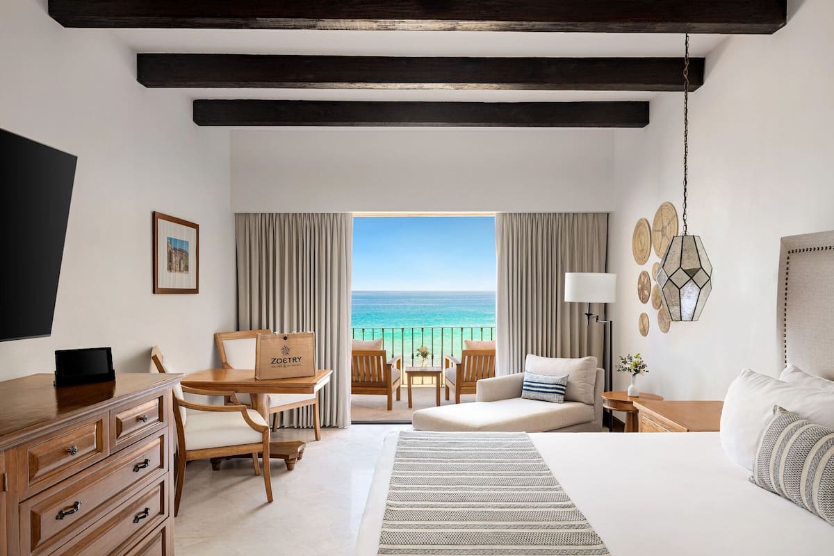 A hotel room with a bed, a desk, a chair, a table, a sofa, and a view of the ocean.