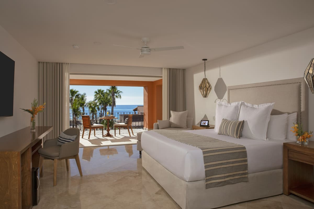 A modern hotel room with a large bed, a desk, and a view of the ocean.