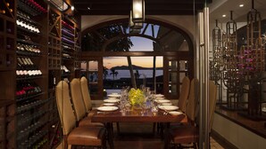 Comedor con una mesa dispuesta para seis personas, rodeada de sillas, con vista al atardecer y montañas al fondo.
