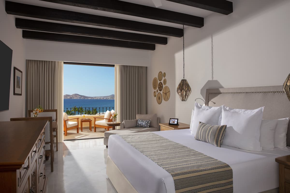 A hotel room with a large bed, a desk, and a balcony with a view of the sea.