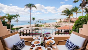 Una mesa de comedor con platos de comida, dos sillas y vistas a la playa y al océano.