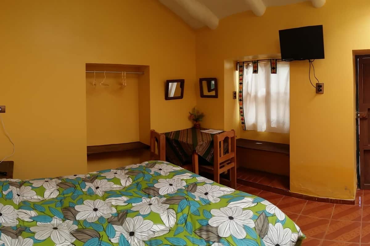 Ein Zimmer mit einem Bett, einem Schreibtisch, einem Stuhl, einem Fernseher und einem fenster mit Vorhängen.