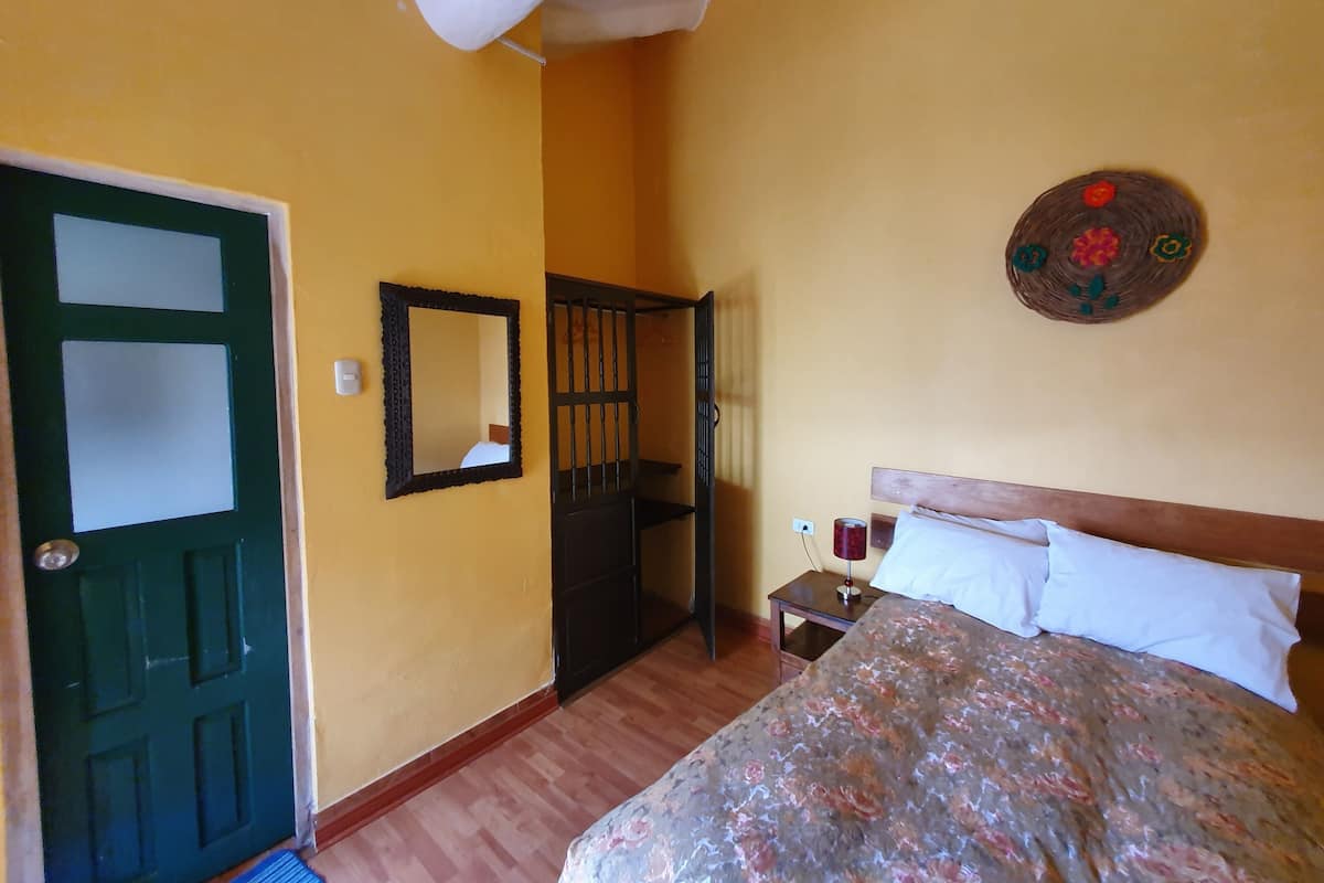 Ein Schlafzimmer mit Bett, Holz-Kopfteil, Nachttisch, Spiegel, Tür und Wandbild.