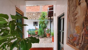 A narrow corridor with a tiled floor leading to a set of wooden stairs. There are potted plants and a bench in the background. - Hospedaje Familiar Kitamayu (Pisac)
