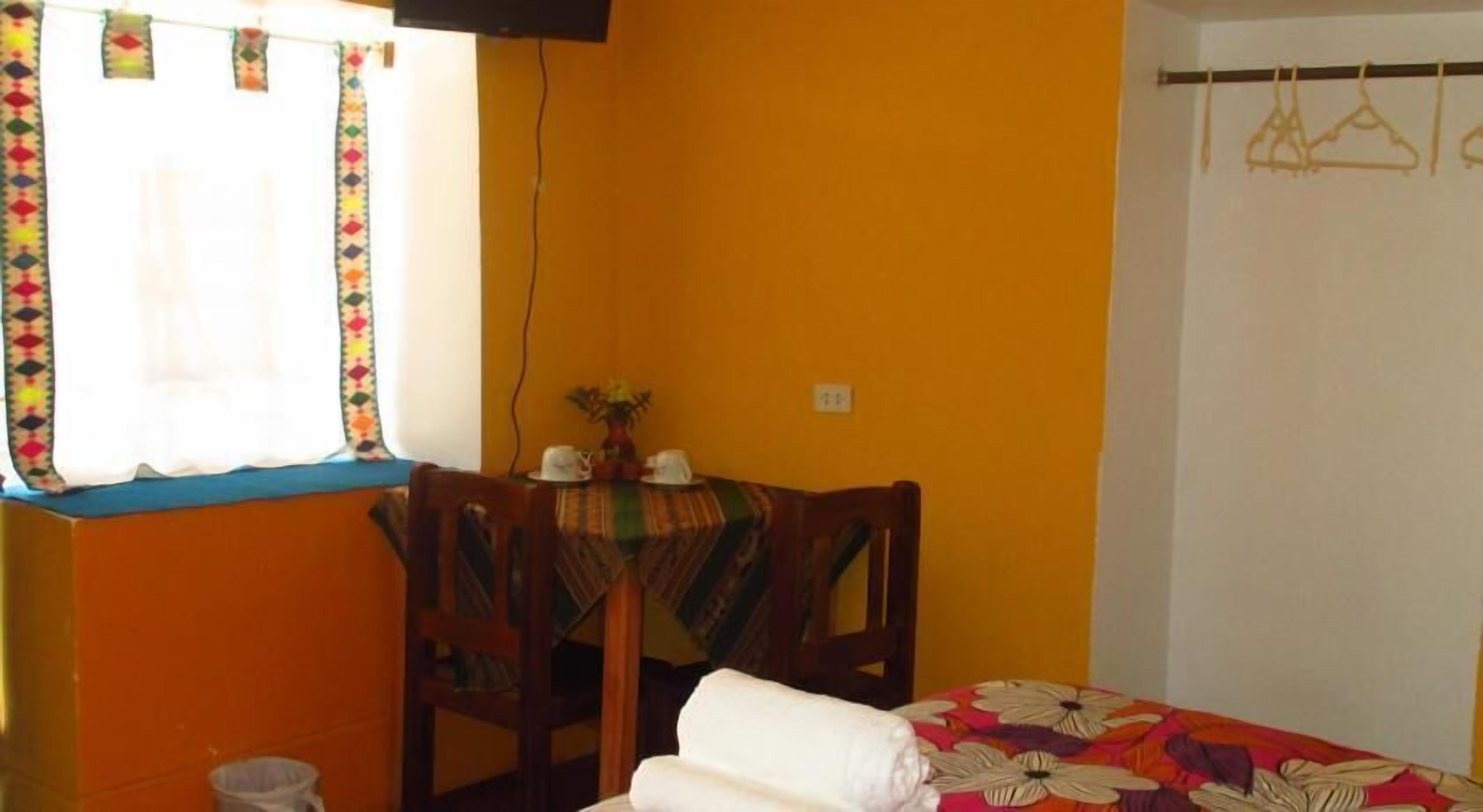 Una habitación con una cama, una mesa con sillas, una ventana con cortinas y un enchufe en la pared.
