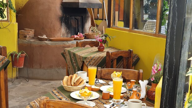A traditional breakfast setup with bread, fruit, and beverages on a patterned tablecloth. - Hospedaje Familiar Kitamayu (Pisac)