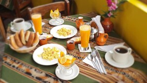 A breakfast table set with plates of food, glasses of orange juice, and a coffee cup. - Hospedaje Familiar Kitamayu (Pisac)