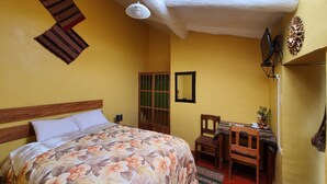 A room with a bed, a desk, and a chair. There is a window with a view of the outside. - Hospedaje Familiar Kitamayu (Pisac)