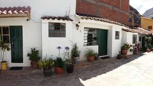 A narrow street with white buildings, green doors, and potted plants. - Hospedaje Familiar Kitamayu (Pisac)