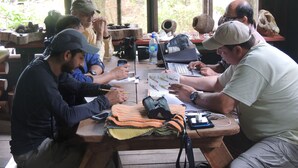 A group of people seated at a wooden table with laptops and notebooks, surrounded by natural scenery visible through large windows. - Yatama Ecolodge Sarapiqui (Las Horquetas)