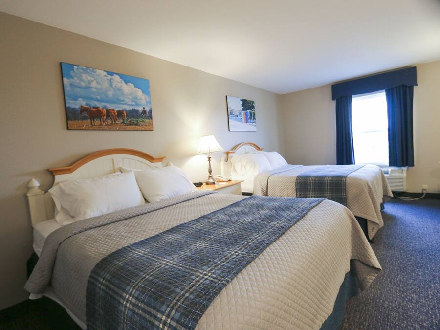 A hotel room with two beds, a painting on the wall, a lamp, and a window with curtains.