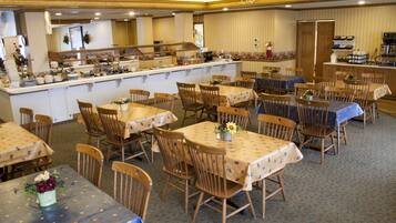 A dining area with multiple tables and chairs, a kitchen in the background, and a bar area.