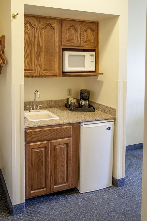 A compact kitchen with wooden cabinets, a white sink, a microwave, and a small refrigerator.