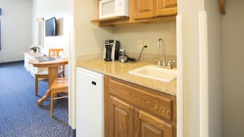 Una cocina compacta con armarios de madera, un microondas, una cafetera y un lavabo.