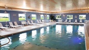 An indoor swimming pool with clear blue water, surrounded by white lounge chairs and tables.