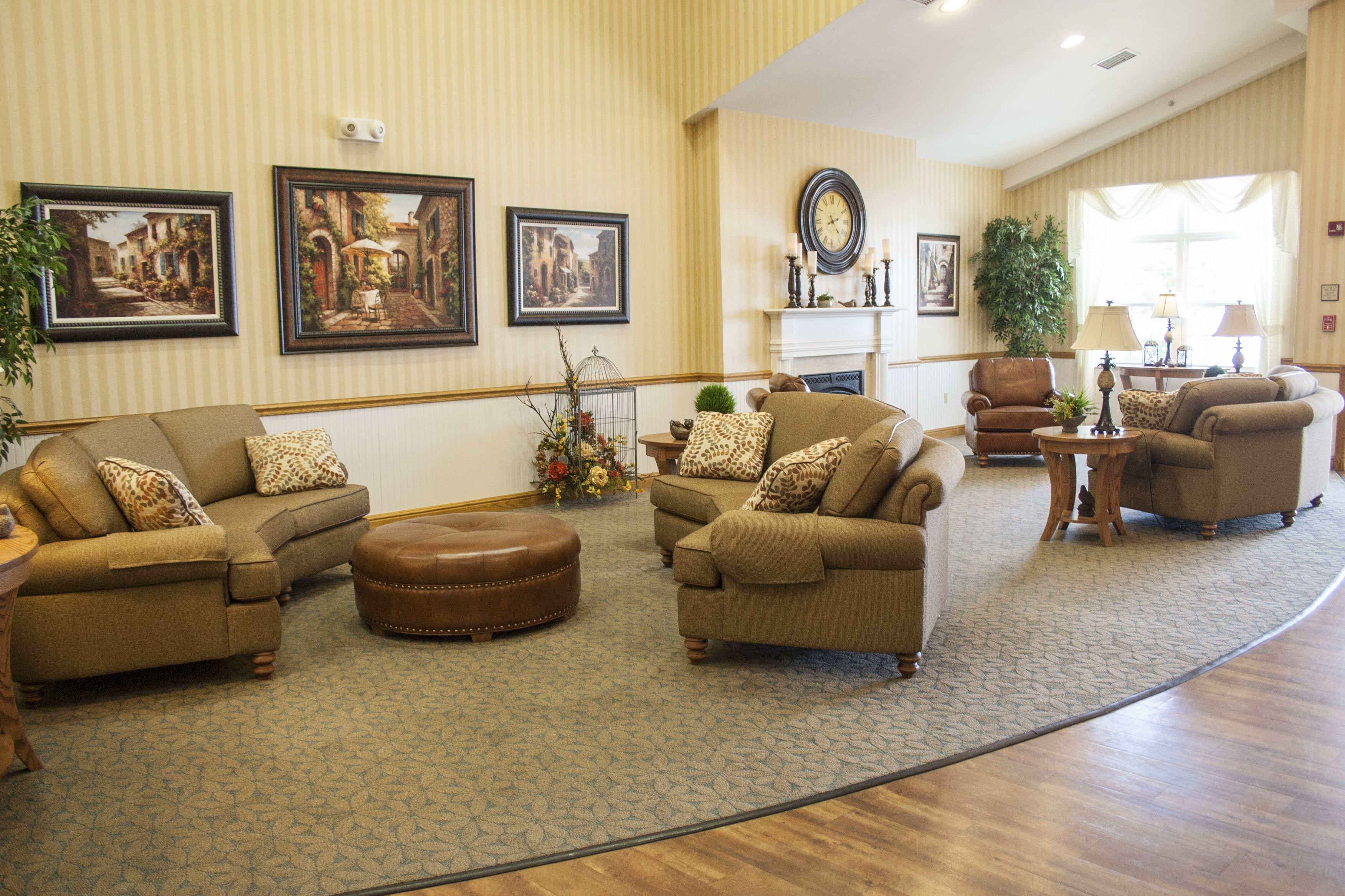 A spacious living room with a large sectional sofa, a round coffee table, and a fireplace. There are framed pictures on the walls and a potted plant in the corner.