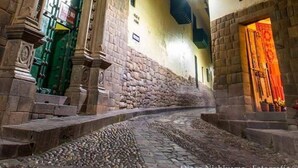 Una calle estrecha con edificios de piedra, un camino adoquinado y puertas iluminadas.