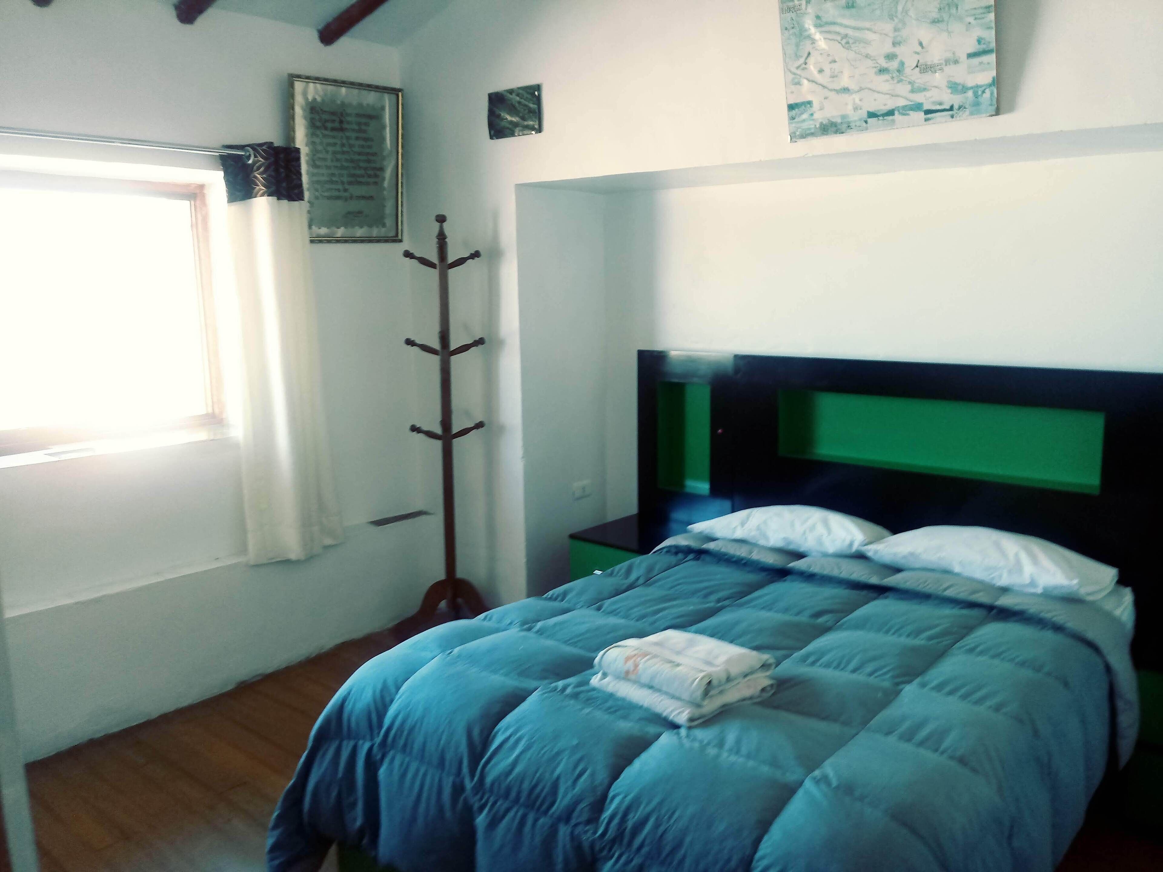 A bedroom with a bed, a coat rack, a window, and a wall with a framed item.