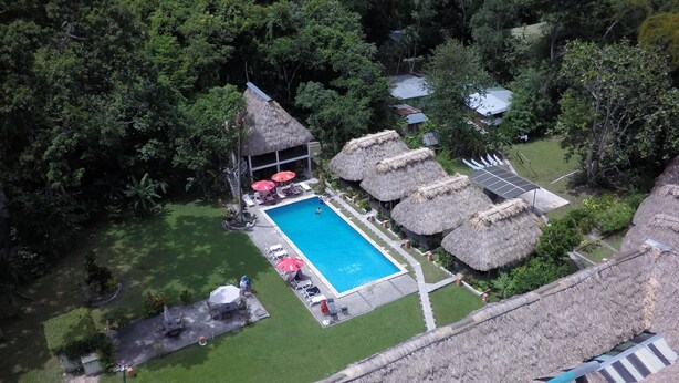 An aerial view of a resort with a swimming pool surrounded by thatched-roof huts and lush greenery. - Hotel Tikal Inn (Flores)