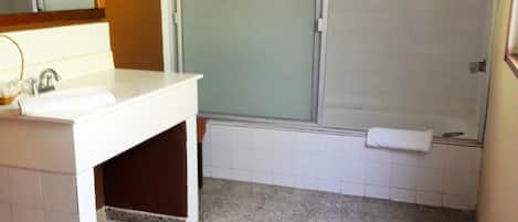 A bathroom with a white sink, mirror, and toilet. There is a shower area with a glass door and a towel hanging on the wall.