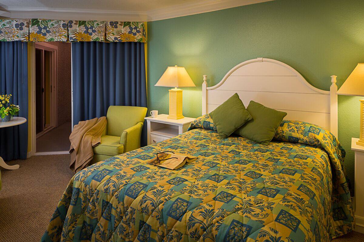 A hotel room with a bed, two bedside tables, a chair, and a door leading to another room.